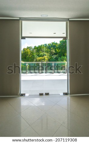 Outlook, view from inside through the glass doors to the modern glass and steel balcony, deck, patio, promenade railing. Exterior, interior design. Vertical.