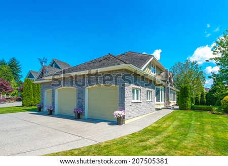 Custom built luxury house with three garage doors and nicely trimmed and landscaped front yard, lawn in a residential neighborhood. Vancouver Canada.