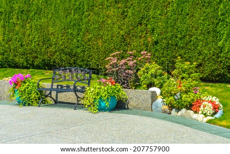 Nicely decorated yard, lawn. Garden bench and flowers in the decorative pots and stones for flowerbed in front of the house, front yard. Landscape design.