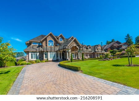 Big custom made luxury house with nicely landscaped front yard and paved driveway to garage in the suburbs of Vancouver, Canada.