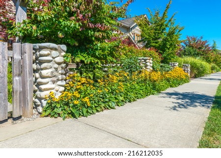 Nicely decorated side of pedestrian sidewalk, yard. Flowers and stones in front of the houses. Landscape design.