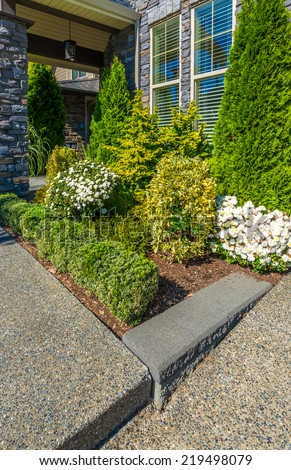 Nicely decorated colorful flowerbed and trimmed bushes at front yard lawn in front of the house. Landscape design. Vertical.