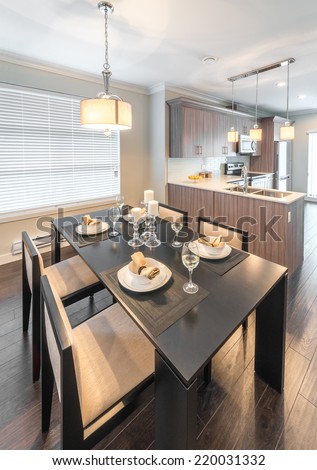 Luxury dining site. Nicely decorated dining table with napkins on the plates and the kitchen on the  back. Interior design of a brand new house. Vertical.