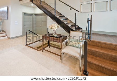 Fragment of the luxury spacious modern room with the stairs to the upper level and table with the chair. Interior design.