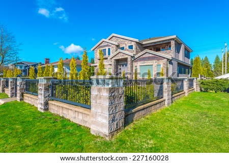 Big custom made luxury house behind the fence with nicely trimmed and landscaped front yard lawn in the suburbs of Vancouver, Canada.