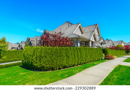 Big custom made luxury house with nicely landscaped front yard behind green fence  in the suburbs of Vancouver, Canada.