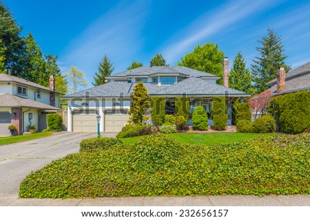 Custom built luxury house with nicely trimmed front yard, lawn, behind green fence and driveway to garage in a residential neighborhood. Vancouver Canada.
