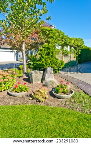 Flowers and stones and nicely trimmed bushes in front of the house, front yard. Landscape design. Vertical.