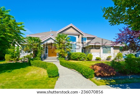 Big custom made luxury house with nicely landscaped and trimmed front yard and long doorway in the suburbs of Vancouver, Canada.