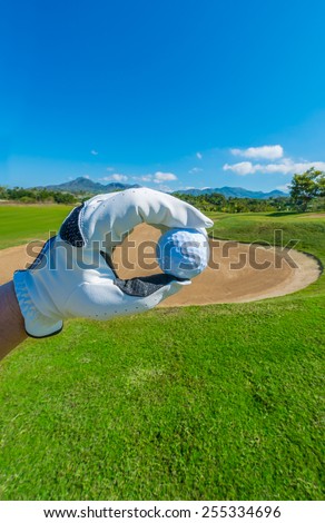 Hand wearing golf glove holding golf ball over beautiful golf course with blue sky.g