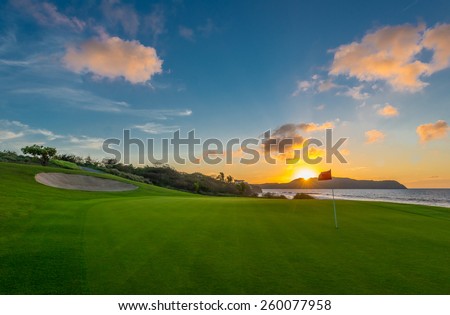Red flag and sand bunker at the beautiful golf course at the ocean side at sunset, sunrise time.