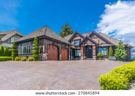 Big custom made luxury house with nicely landscaped front yard and long and wide paved driveway to the triple doors garage in the suburb of Vancouver, Canada.