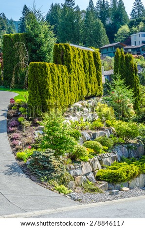 Trimmed bushes, flowers and stones in nicely decorated front yard of the house. Landscape design.