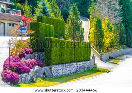 Nicely trimmed bushes, green fence and lowers and stones on different levels in front of the house, front yard. Landscape design.
