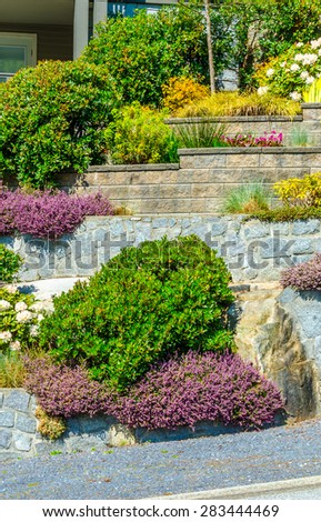 Flowers and stones on different levels in front of the house, front yard. Landscape design. Vertical.