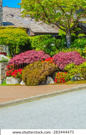 Trimmed bushes, flowers and stones in nicely decorated front yard, lawn of the house. Landscape design. Vertical.