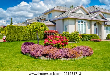 Big custom made luxury house with bushes, flowers and stones in nicely decorated front yard, lawn of the house.