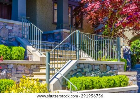 House entrance with nicely paved doorway, steps and handrails and trimmed and landscaped front yard.