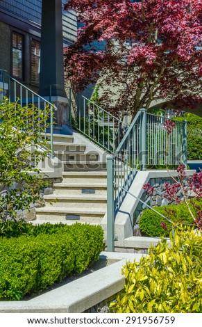 House entrance with nicely paved doorway, steps and handrails and trimmed and landscaped front yard. Vertical.