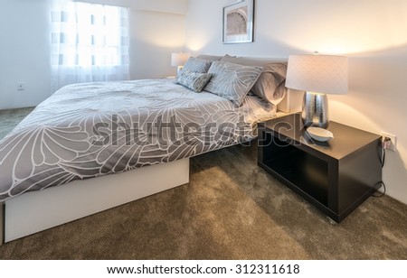 Modern comfortable and elegant luxury master bedroom with the night stand and the lamp on it. Interior design.