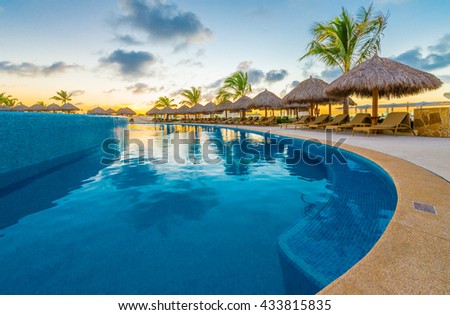 Swimming pool and a grass beach umbrellas with lounges at night, dawn, evening time at the luxury Caribbean, tropical resort.