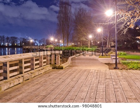 Fantastic view of the wooden trail,  promenade, road, path in the park along the river ( ocean ) bank at night, dick time. Vancouver, Canada