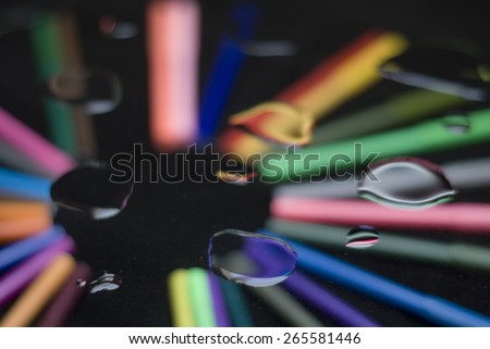 Close up on water drops above a quarter circle of colourful felt tip pens isolated on black