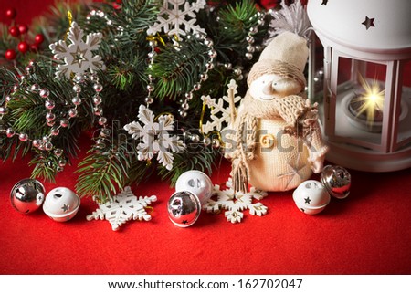 Cute little adorable snowman is standing near the white fairy lantern and decorated fir tree branch behind it. Christmas card with copy space for your text.