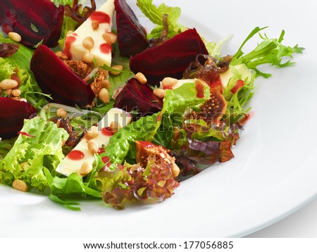 Fresh vegetarian gourmet salad with baked beetroot and cheese served on a white round plate. Isolated on white.