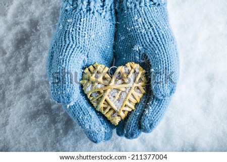 Woman hands in light blue knitted mittens are holding a beautiful glossy red heart in a snow background. Love and St. Valentine concept.