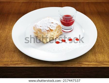 Delicious and yummy Napoleon cake with confectioners sugar and  berry topping on a round plate on wooden table