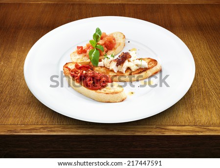 Assorted bruschetta with salmon, air-dry tomatoes or goat cheese served with the basil leaf on a round white plate on wooden table