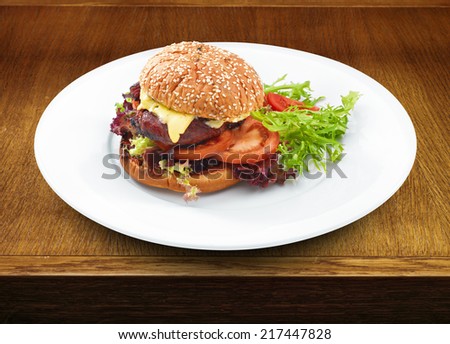 Fresh tasty hamburger with geilled patty and cheese served with vegetables. Wooden table