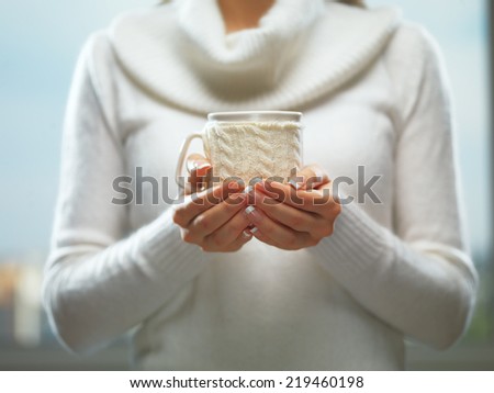 Woman holds a winter cup close up. Woman hands with elegant french manicure nails design holding a cozy knitted mug. Winter and Christmas time concept.