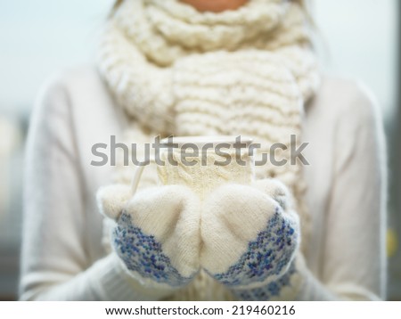 Female hands holding knitted winter mug close up. Woman hands in white and blue mittens holding a cozy knitted cup with hot cocoa, tea or coffee. Winter and Christmas time concept.