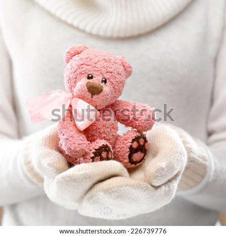 Female hands holding a cute teddy bear. Woman hands in white mittens showing a teddy bear gift dresses in  knitted hat and scarf. Cute Christmas present. Winter holidays concept.