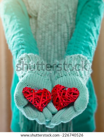 Female hands in light teal knitted mittens with entwined red heart Love and St. Valentines Day concept.