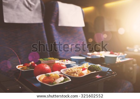 Tray with delicious healthy food on the plane, business class travel. Tasty Lunch served in the aircraft interior. Sun shining through the airplane window. Lens Flare.