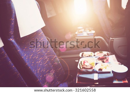 Tray with delicious healthy food on the plane, business class travel. Tasty Lunch served in the aircraft interior. Sun shining through the airplane window. Lens Flare.