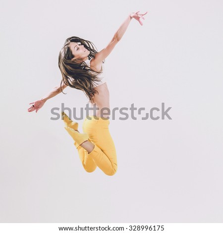 Young dancer woman jumping on a studio background. Healthy athletic woman is practicing dancing moves and jumps in the studio. Professional ballet dancer. Active sports lifestyle concept.
