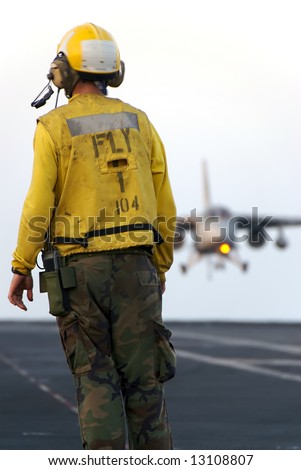A sailor watches as a naval aircraft lands aboard an aircraft carrier