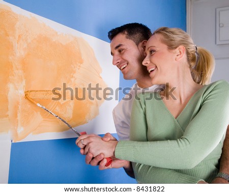 young married couple painting walls of their new home