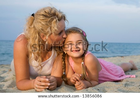 mother kissing her little daughter at the beach while having summer holiday