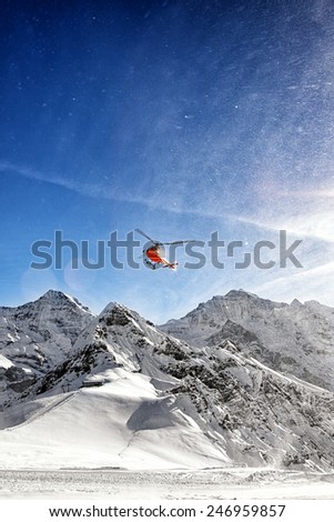 Red helicopter in flight in winter alps with snow powder near winter resort