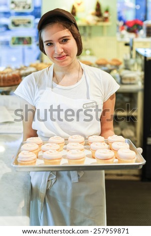 Smiling shy girl in the cap with cupcakes at the tray in the bakery
