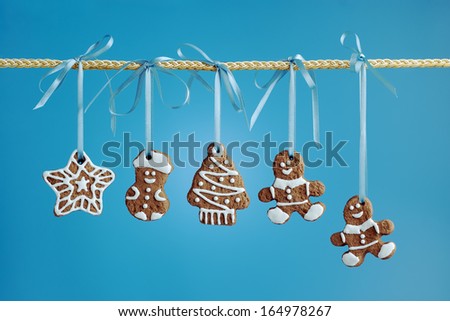 Christmas gingerbread cookies of various shapes hanging on a ribbon on a blue background.