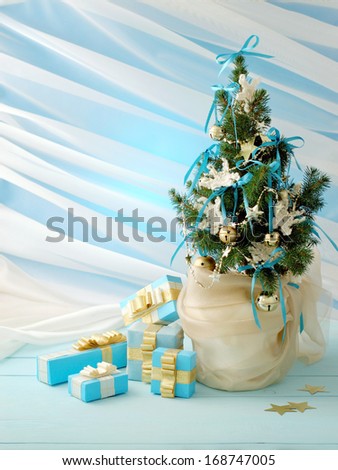 Christmas tree decorated with golden bells, crocheted snowflakes and blue ribbons with gifts on a blue background.