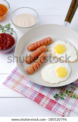 Fried eggs and three sausages in a ceramic pan vertical format.