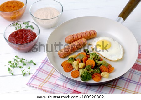 Fried eggs with sausages and mixed vegetables in a ceramic pan.