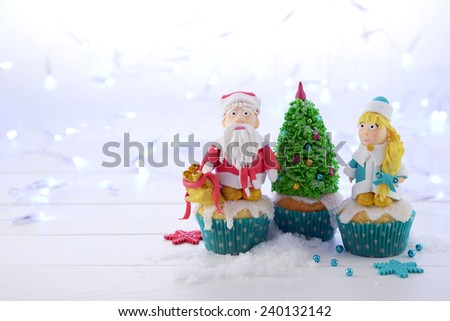 Cupcakes decorated with sugar Santa Claus Snow Maiden and Christmas tree on the Christmas lights background.